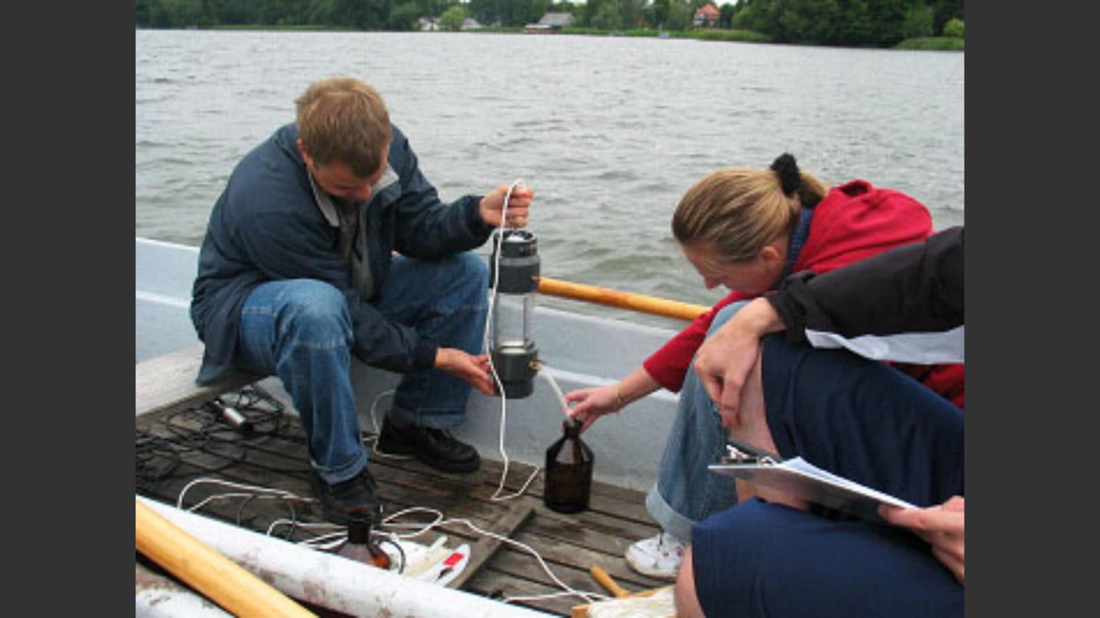 Mitarbeitende des Studienprojekts sitzen in einem Boot auf dem See und führen eine Wasseranalyse durch