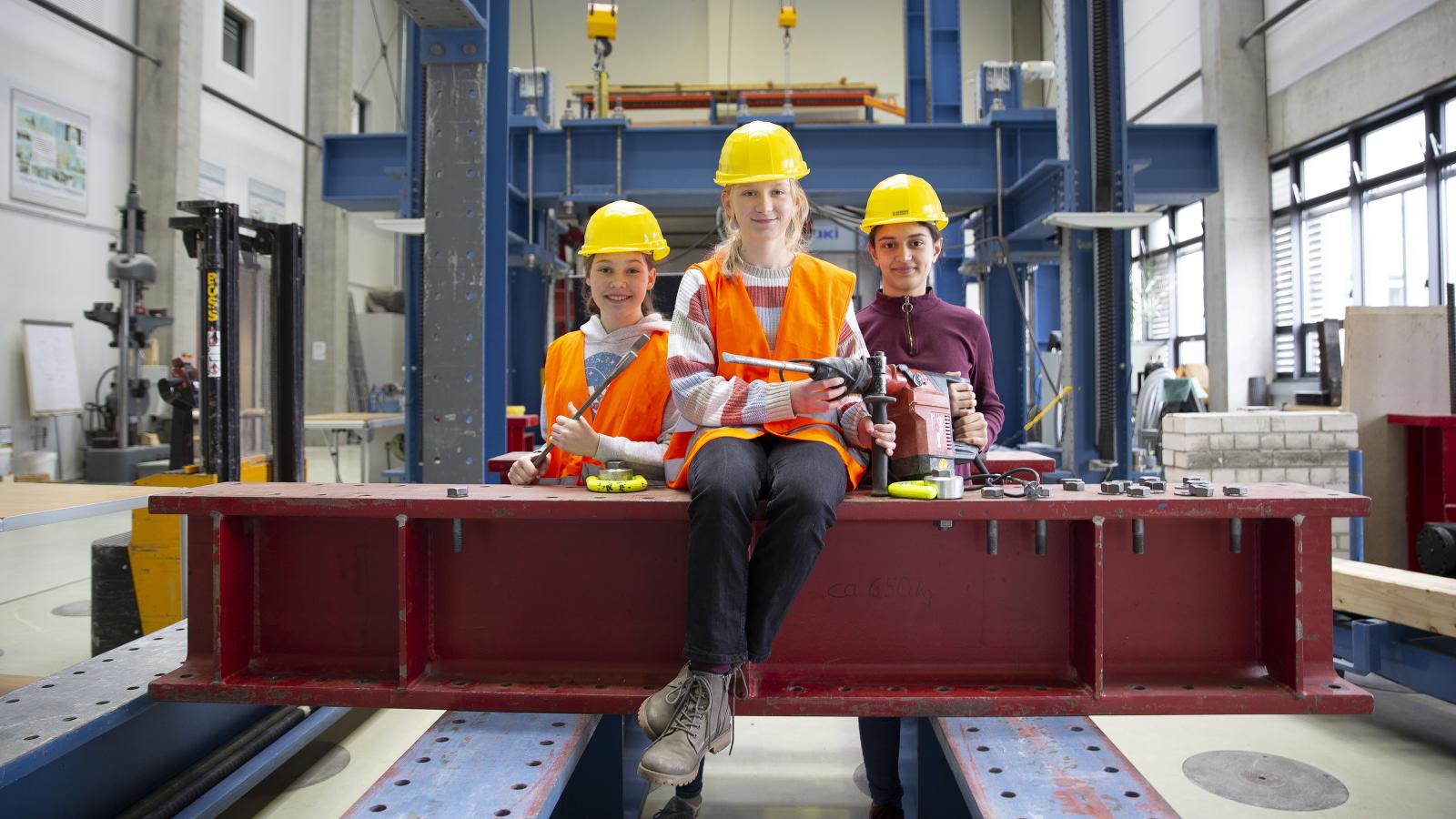 Schülerinnen sitzen mit Werkzeugen und Bauhelmen ausgestattet in einer Werkstatt der FH Potsdam
