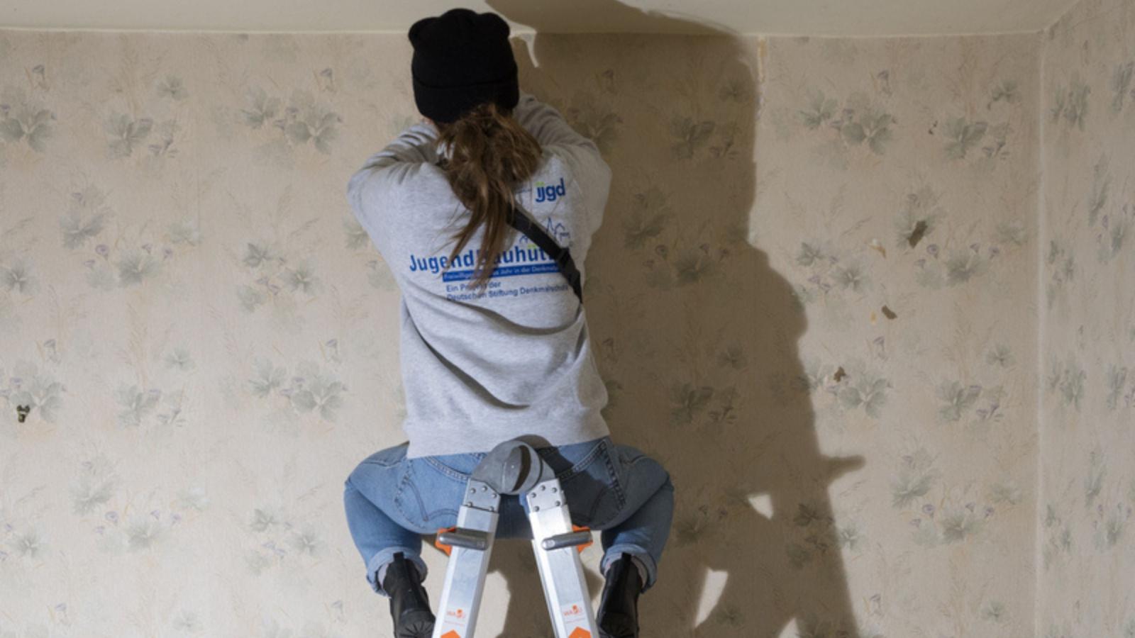 Eine Frau sitzt auf einer Leiter und untersucht die Decke eines Raumes