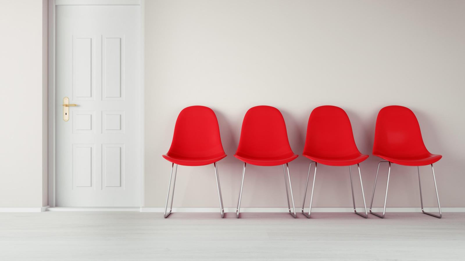 Vier rote Stühle in einem Wartezimmer vor einer geschlossen weißen Tür