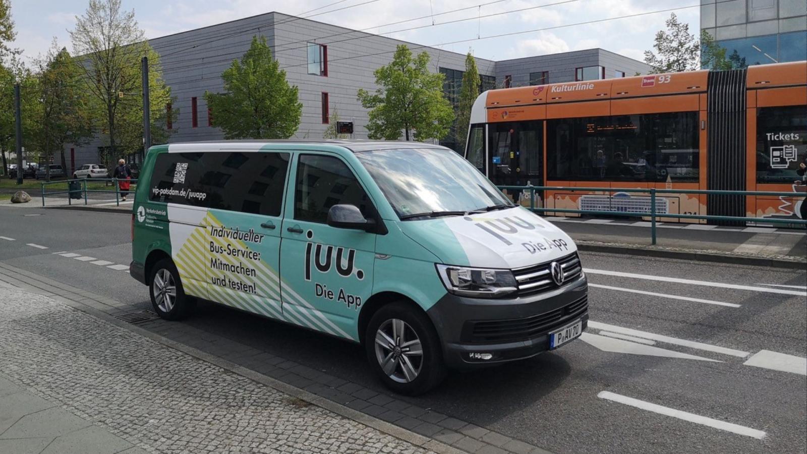 Der Minibus "Juu-Limo" steht auf der Straße vor der Straßenbahnhaltestelle Fachhochschule. Im Hintergrund befindet sich eine einfahrende Tram sowie das Hauptgebäude der Fachhochschule Potsdam