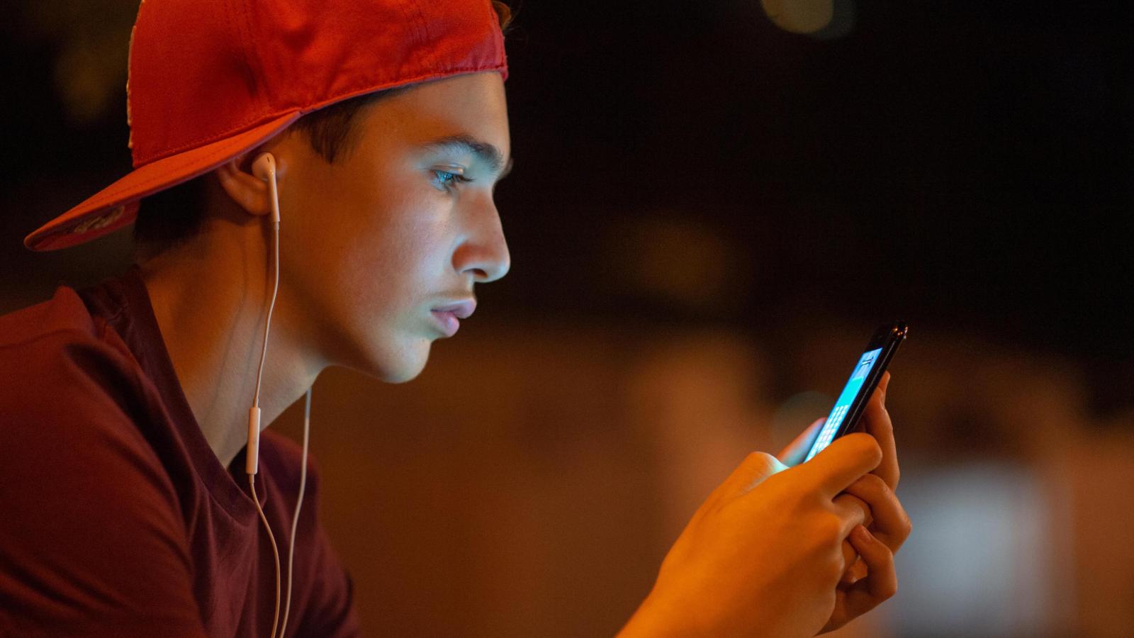 Junger Mann mit roter Basecap schaut auf sein Smartphone.