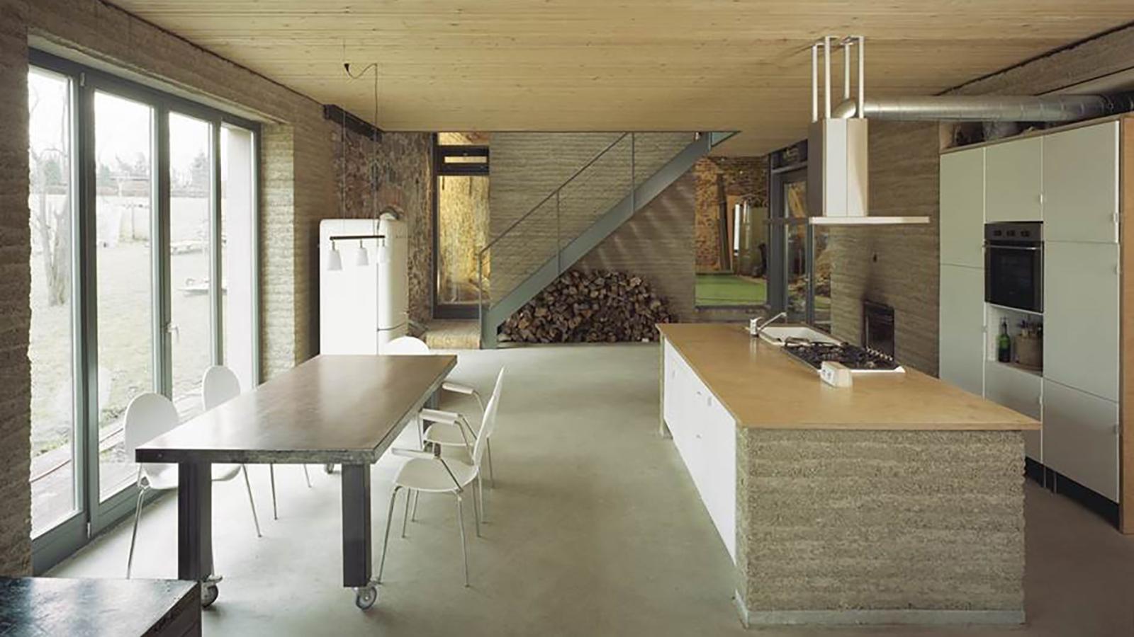 Stampflehmhaus: Modern eingerichtetes Zimmer mit Küche, Esstisch und Fensterfront