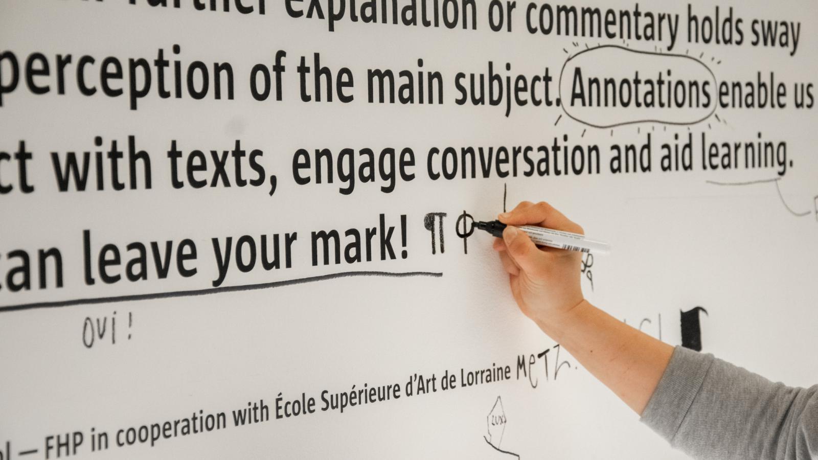 Foto von Hand, die gerade etwas an die Wand schreibt mit einem schwarzen Stift