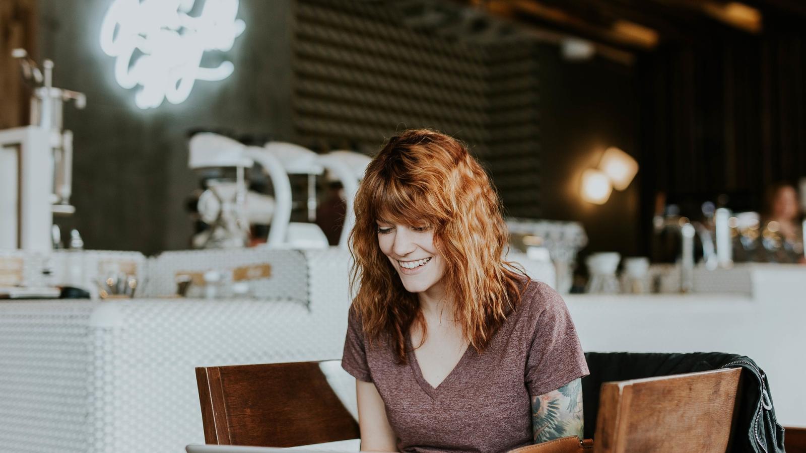 Frau sitzt lächelnd am Laptop im Café 