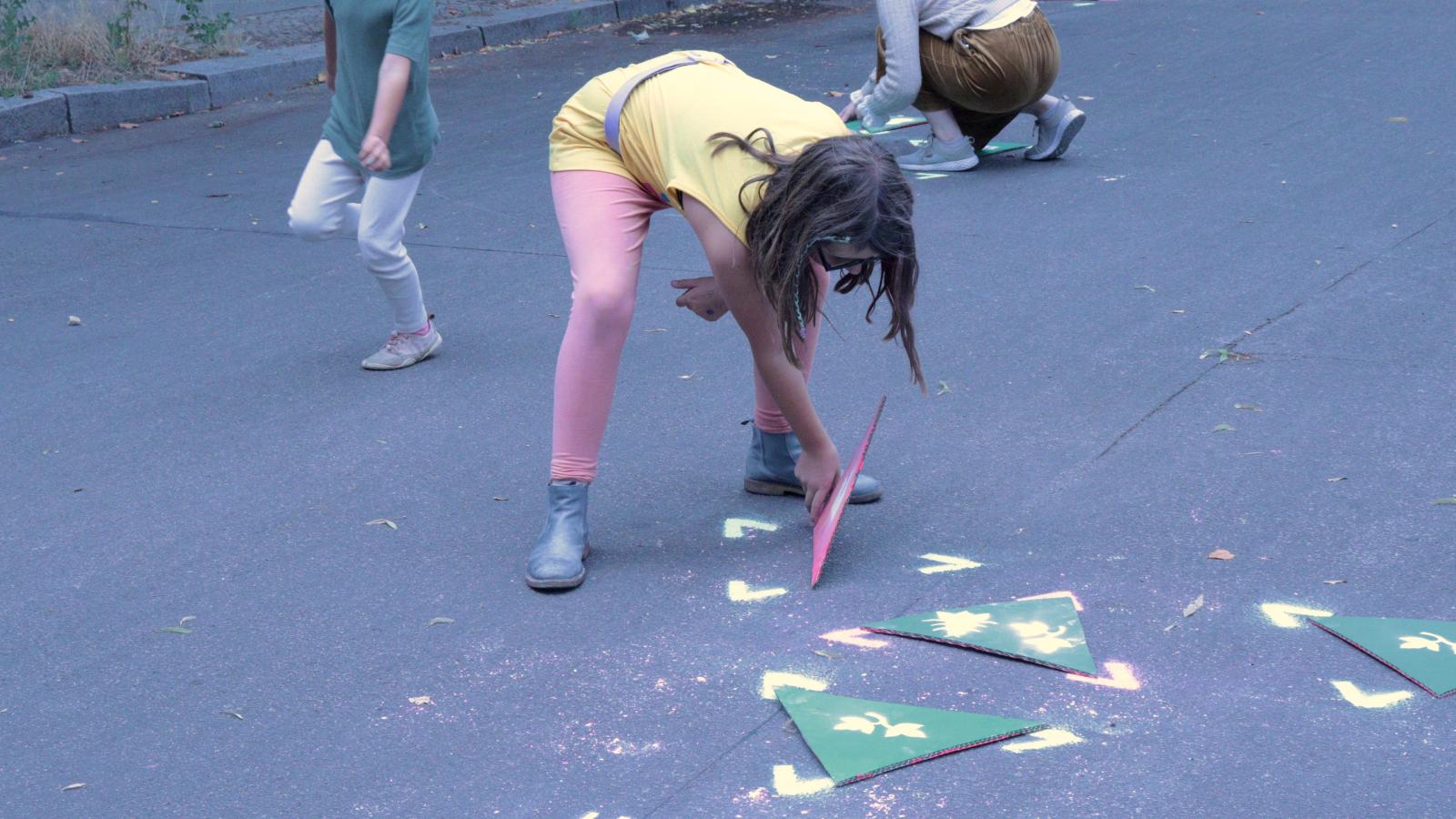 Kinder spielen mit grünen Dreiecken aus Pappe auf dem Asphaltboden