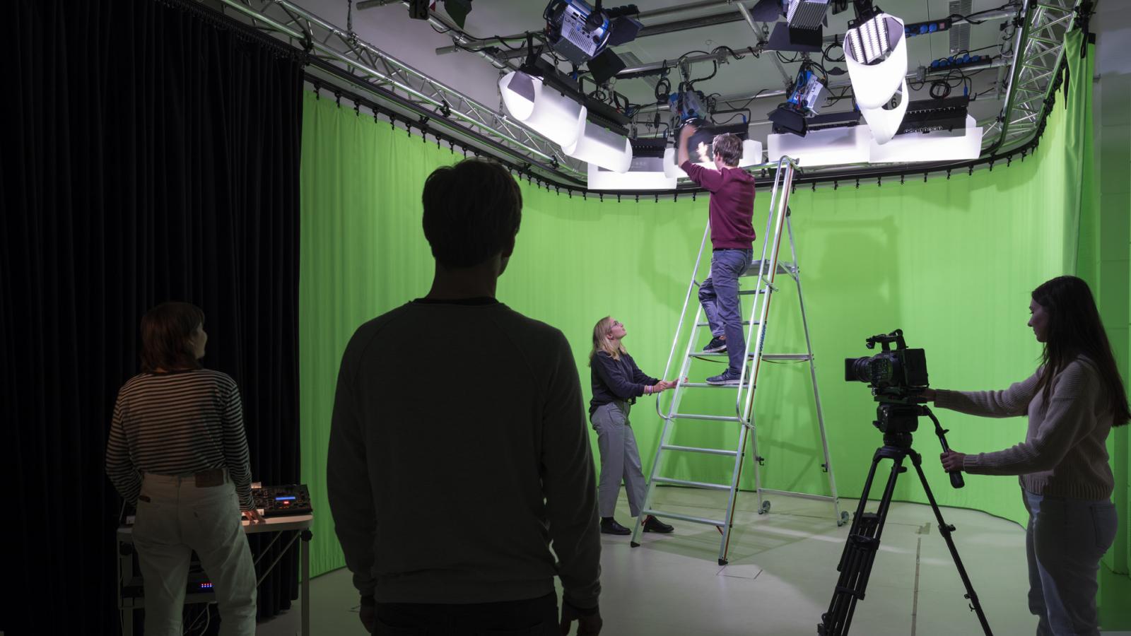 Eine Gruppe Studierender arbeitet zusammen im Videolabor vor einem Greenscreen