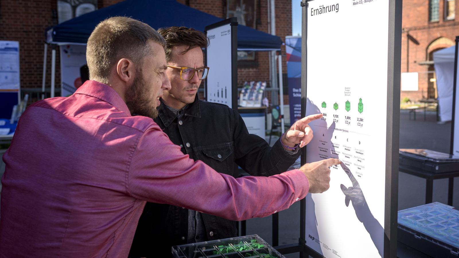 Manuel Jakob (links im Bild), Referent Wissenschafts- und Ausbildungscampus der BahnTechnologie Campus Havelland GmbH, lässt sich von Stefan Aufrichter von der FHP das "Spiel mit Grenzen – Mein persönliches CO2 Budget" erklären 