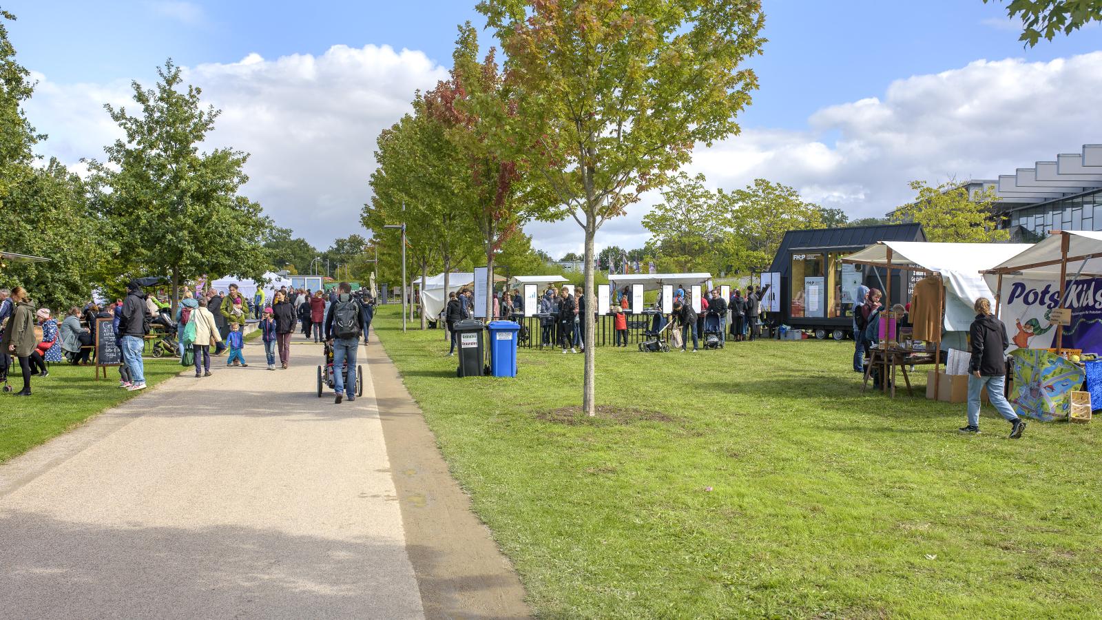 Blick vom Weg aus auf die Ausstellungsstände beim Umweltfest 2022 im Volkspark Potsdam. In der Ferne ist das FHP Mobil zu sehen