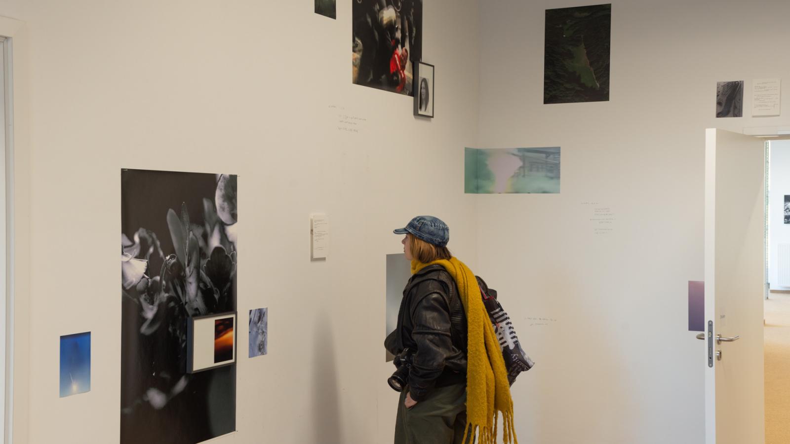 Person steht in einem Raum mit verschieden großen Fotografien collagenartig an den Wänden