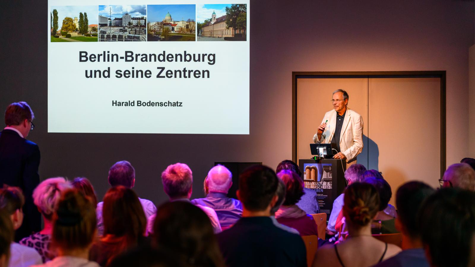 Prof. em. Dr. Harald Bodenschatz hält seinen Vortrag zum Thema "Berlin-Brandenburg und seine Zentren" vor vielen interessierten Besucher*innen der 3. Veranstaltung der Reihe Baukultur und Klimaschutz leben