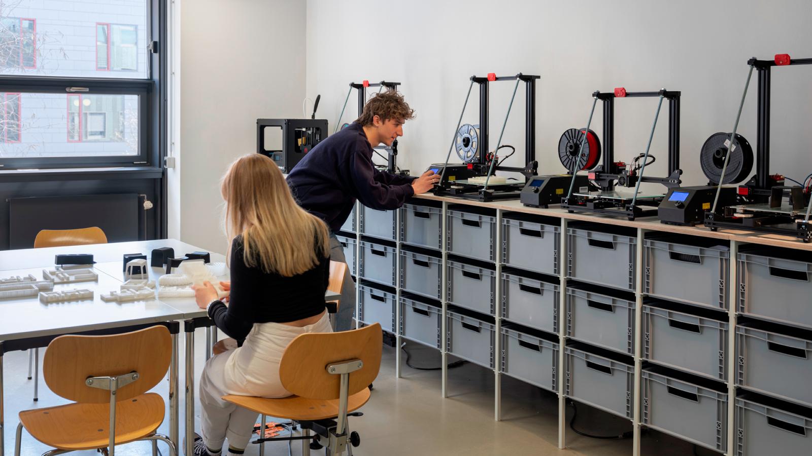 Zwei Studierende vor einer Reihe von 3D-Druckern