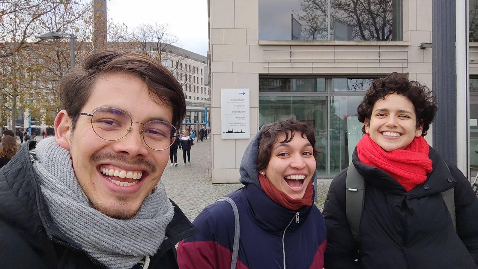 Drei Personen machen ein Selfie. Sie tragen dicke Jacken und Schal und lachen groß.