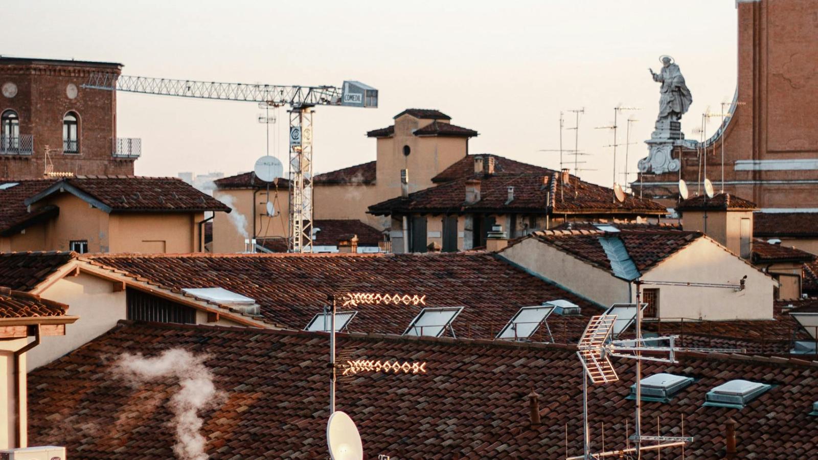 Der Blick führt über die Dächer Bolognas. Ein Kran und eine alte weiße Statue ragen zwischen den Dächern heraus.