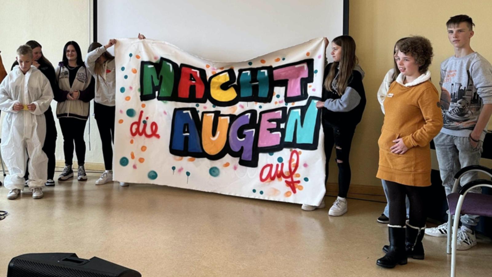 Schüler*innen von Wittenberger Schulen halten ein Plakat mit dem Motto "Macht die Augen auf"