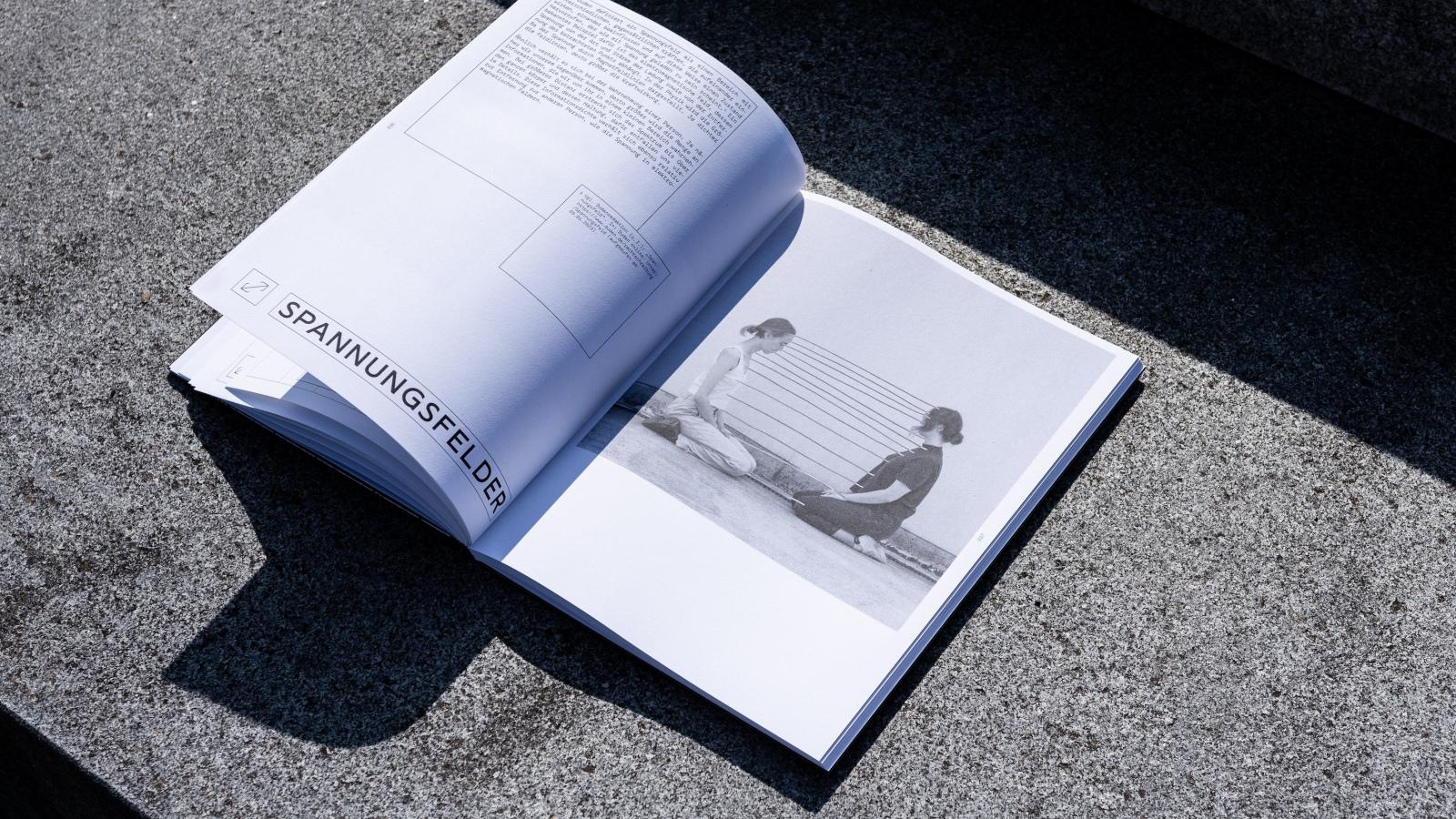 ein aufgeschlagenes Buch mit einem schwarz-weiß Foto von zwei Personen, Text und dem Titel „Spannungsfelder“
