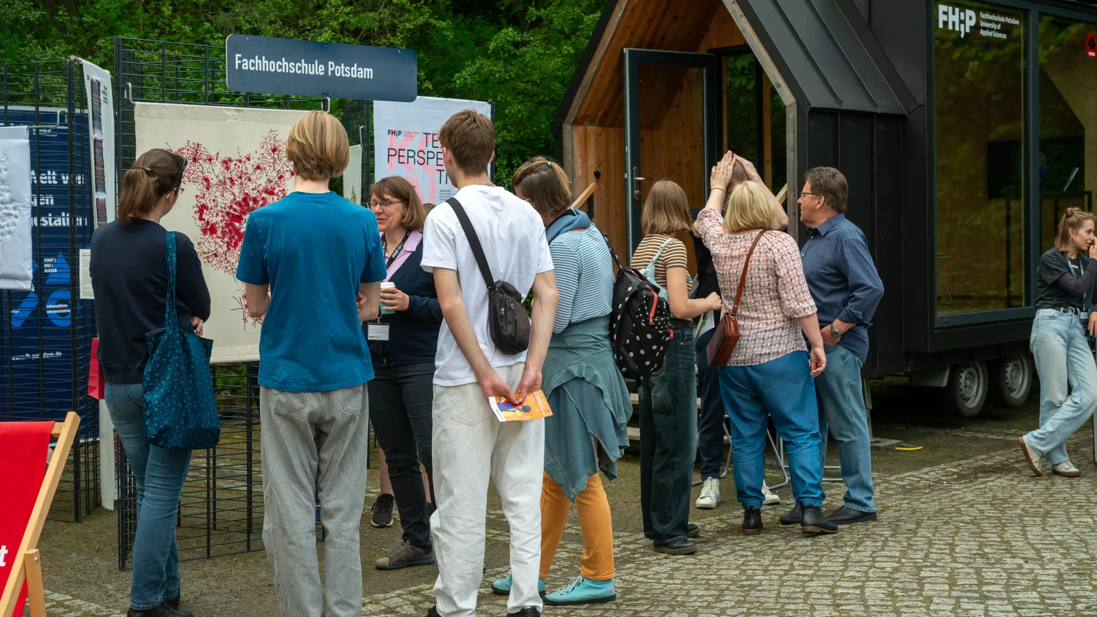 Interessierte Besucherinnen und Besucher beim Potsdamer Tag der Wissenschaften 2024 betrachten die Interface Design Ausstellung vor dem FHP Mobil