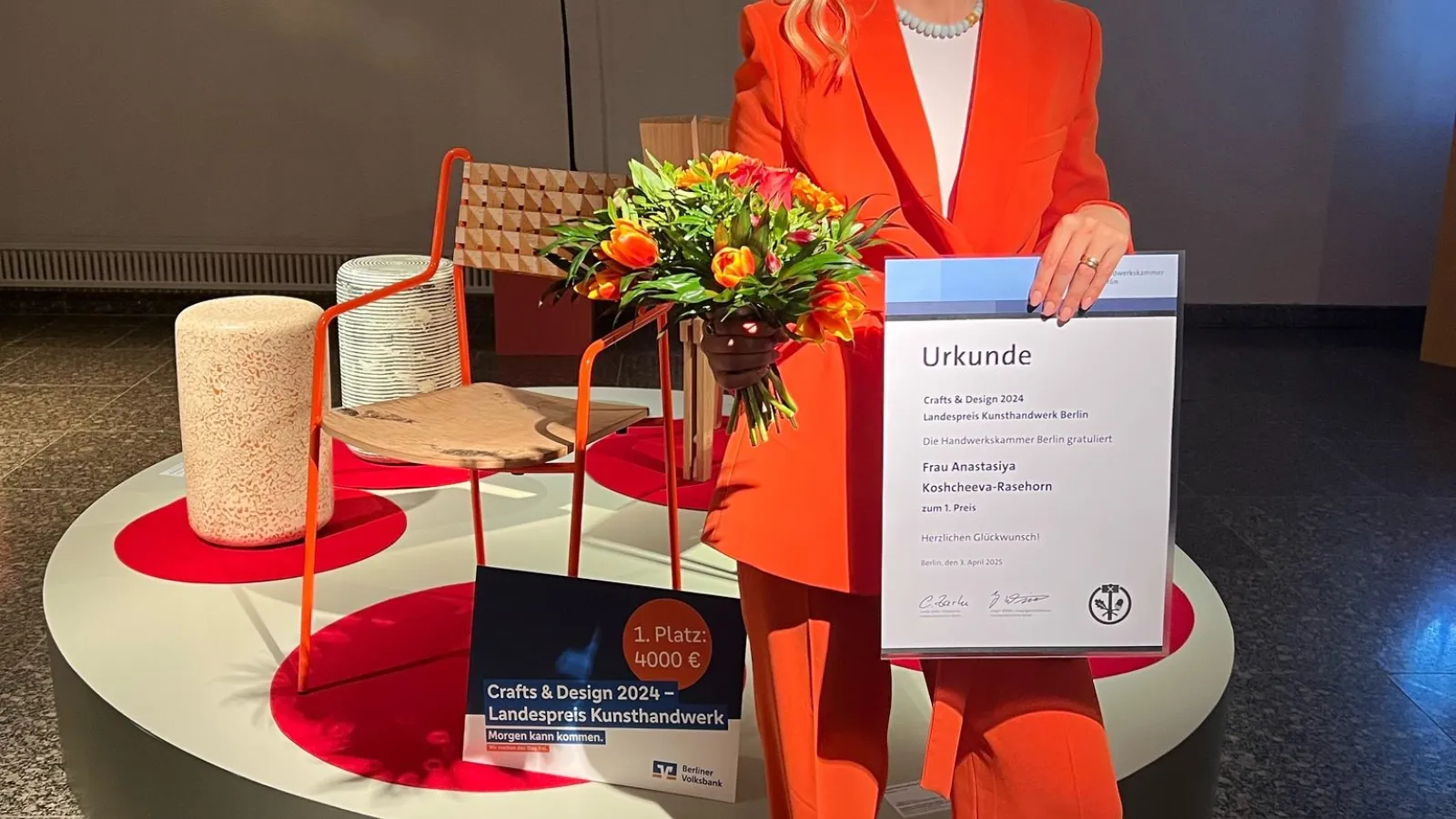 Frontalbild der Designpreis-Gewinnerin in rotem Anzug vor ihrem prämierten Stuhl
