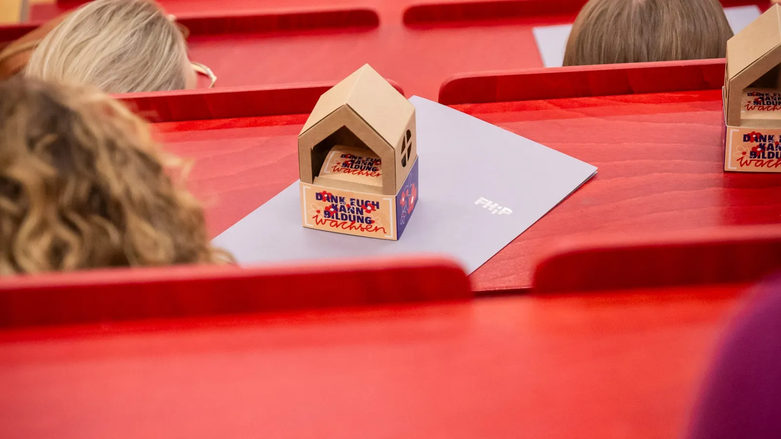 Teilnehmer*innen von hinten sitzend im Hörsaal mit Geschenk