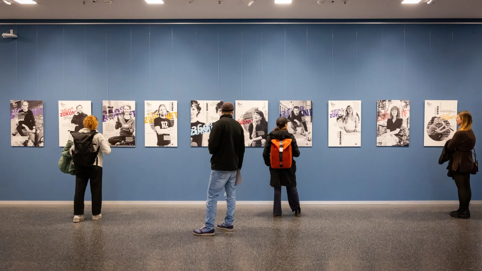 Menschen stehen vor den Porträts an den Wänden und betrachten diese