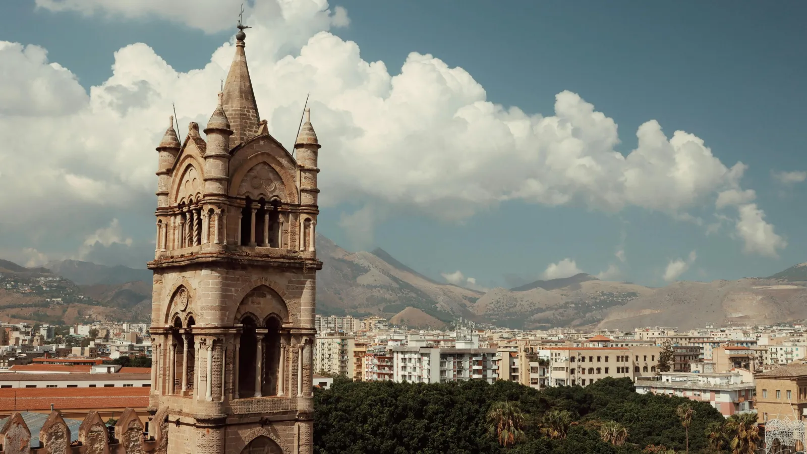Im Vordergrund ist ein alter Kirchturm zu sehen, im Hintergrund ein weiter Blick über die Dächer von Palermo.