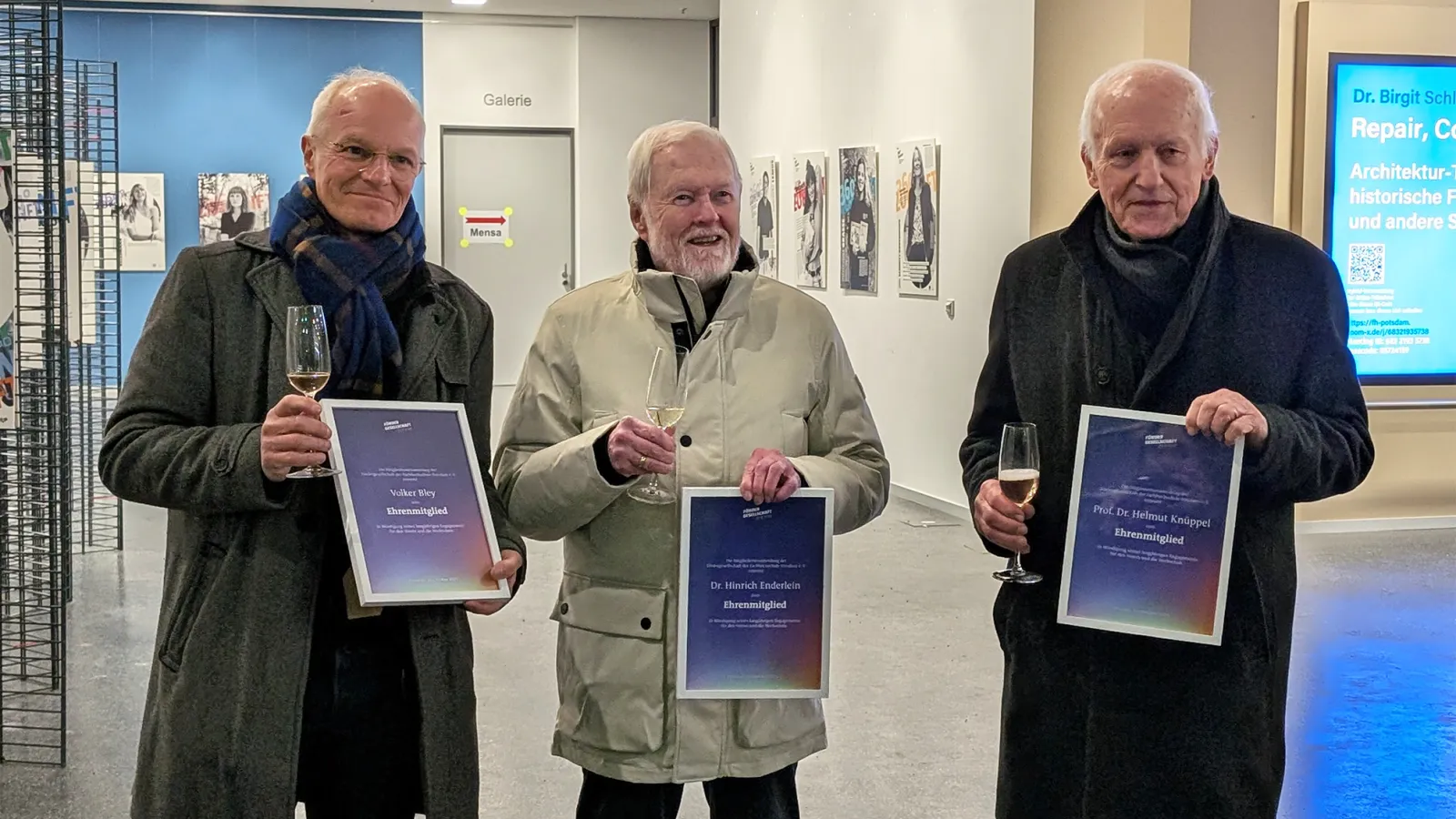 Drei Personen stehen nebeneinander und halten jeweils eine eingerahmte Urkunde in der Hand.