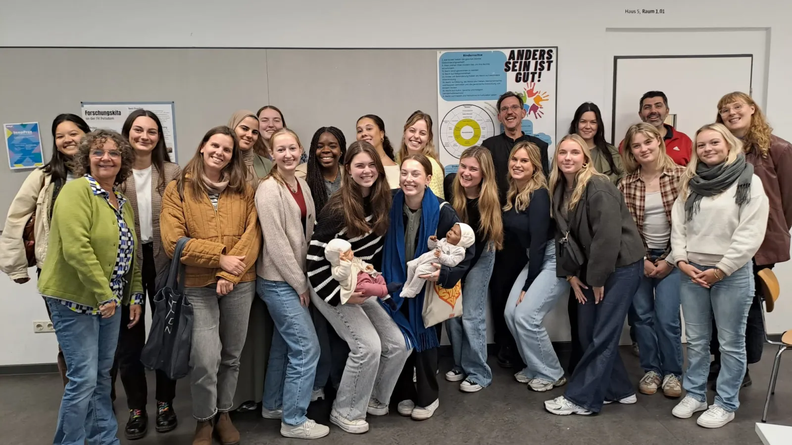 Gruppe von Studierenden in einem Raum, einige halten Puppen, im Hintergrund Plakate an der Wand.