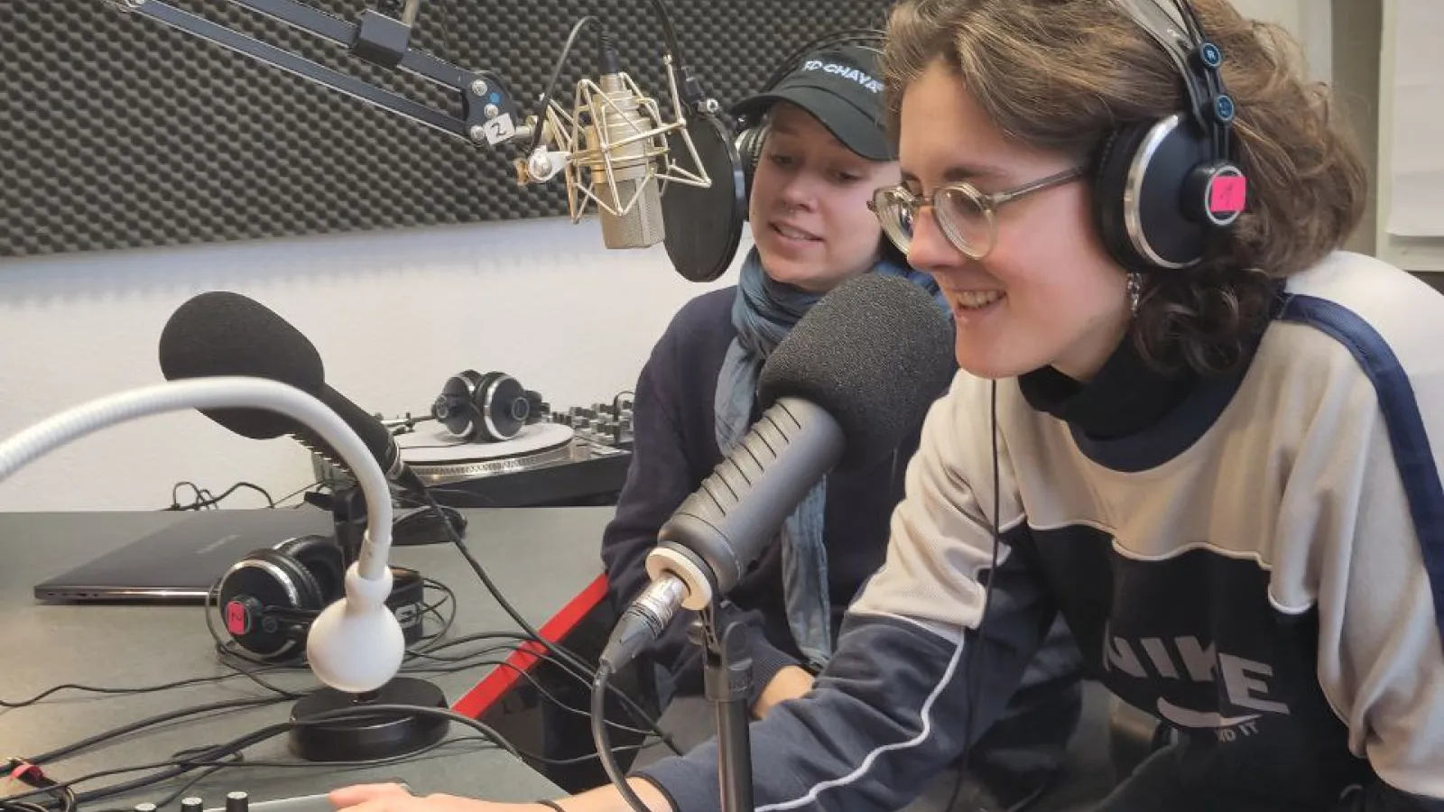 Das Bild zeigt zwei Personen an einem Mischpult mit Mikrophon.