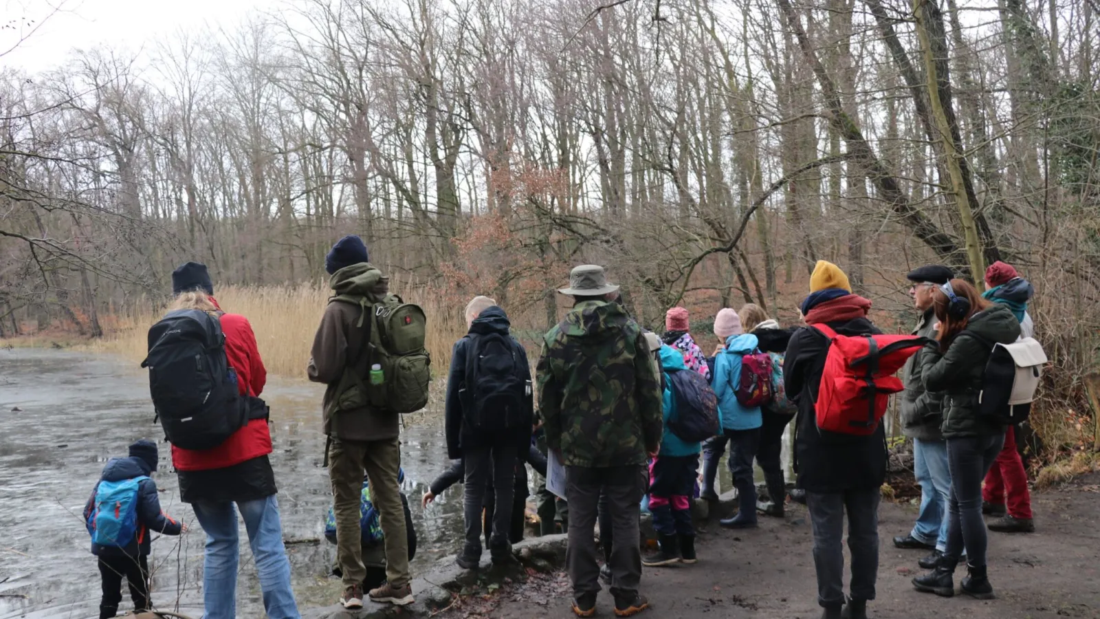 Das Bild zeigt mehrere Personen in der Natur an einem Teich.