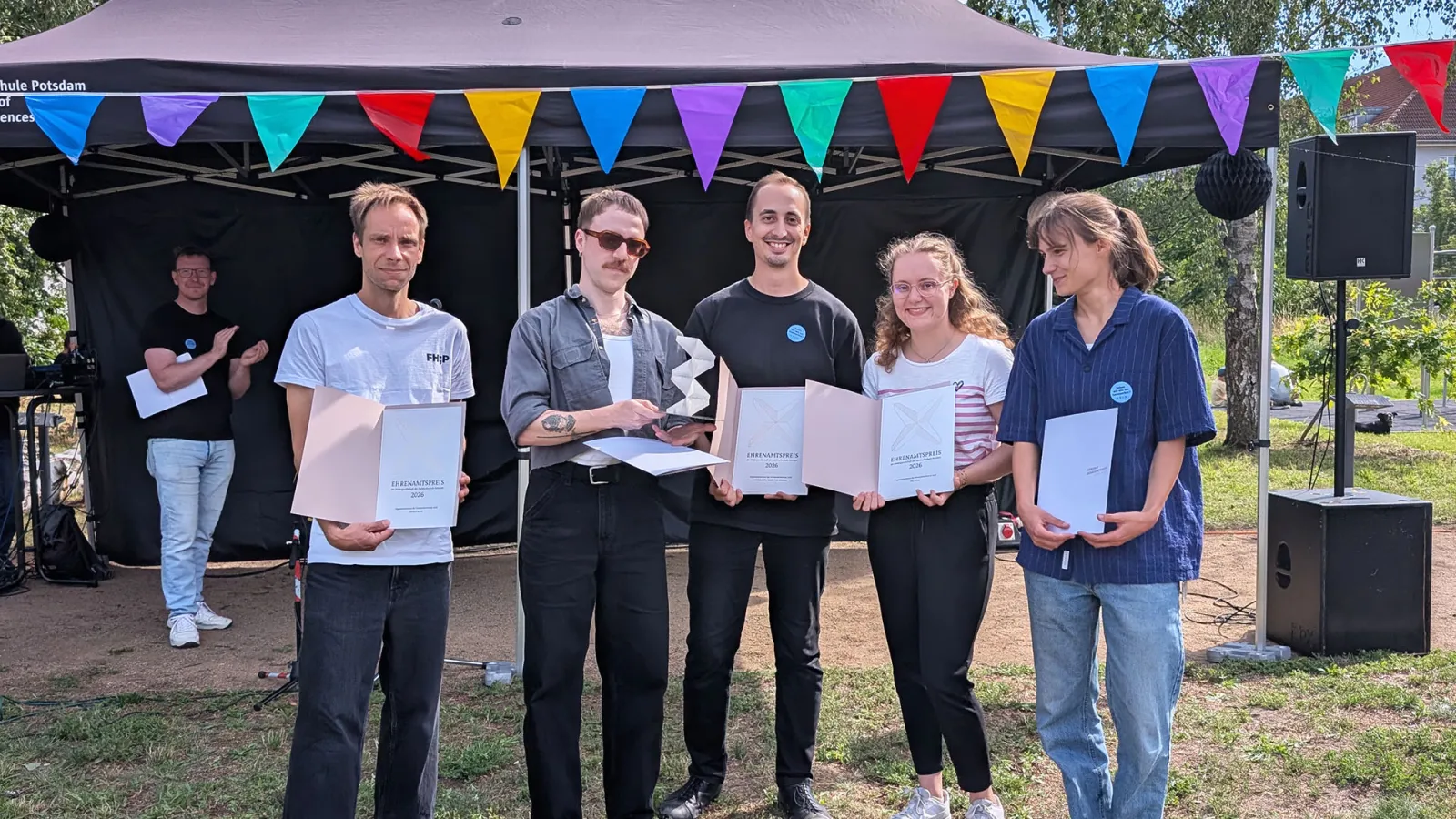 Fünf Studierende halten ihre Urkunden und eine Trophäe auf der Campuswiese.