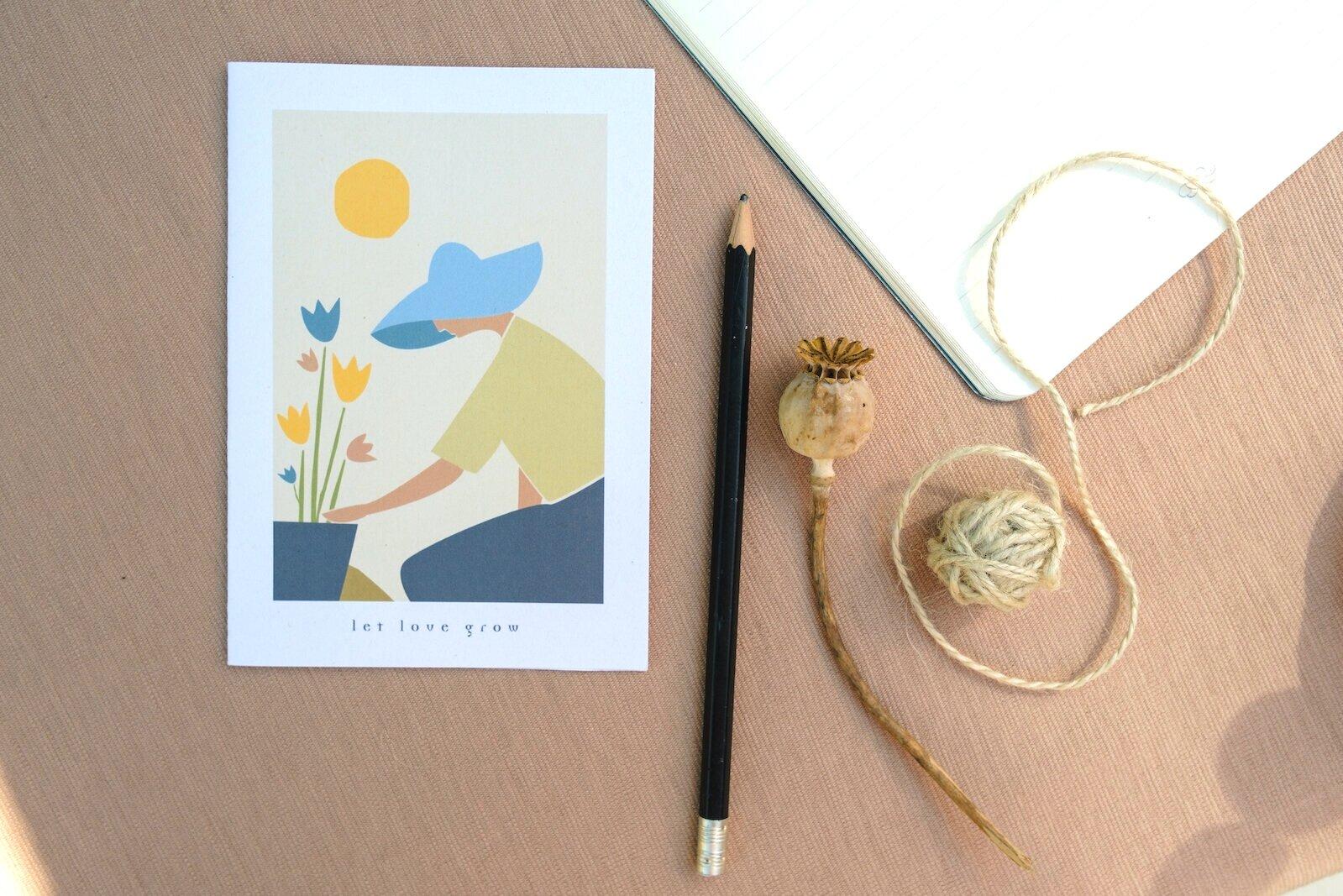 Illustrierte Postkarte daneben Bleistift und Trockenblume
