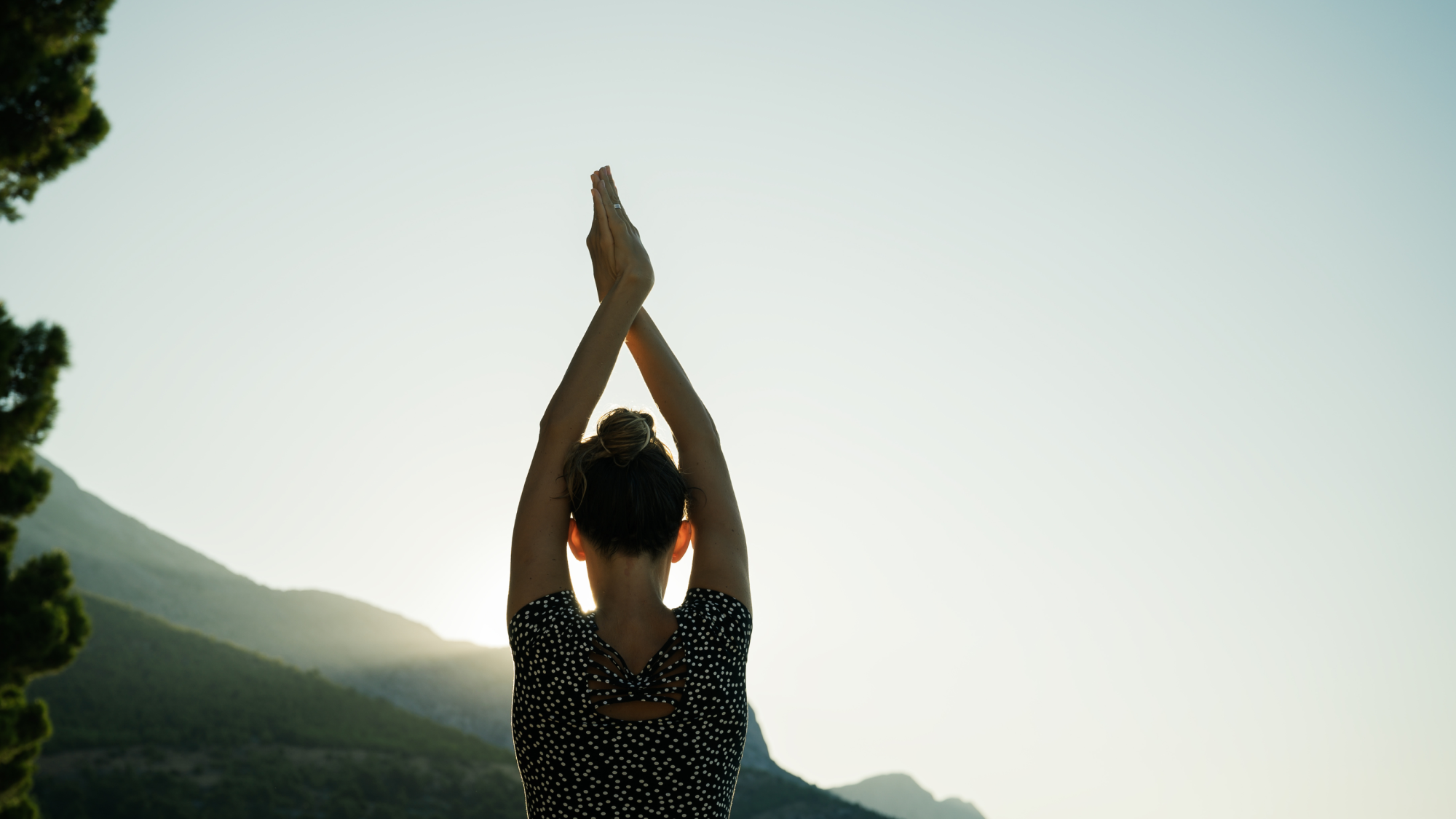 Eine Person in Yogapose hält die Handflächen gegeneinander gedrückt über ihren Kopf