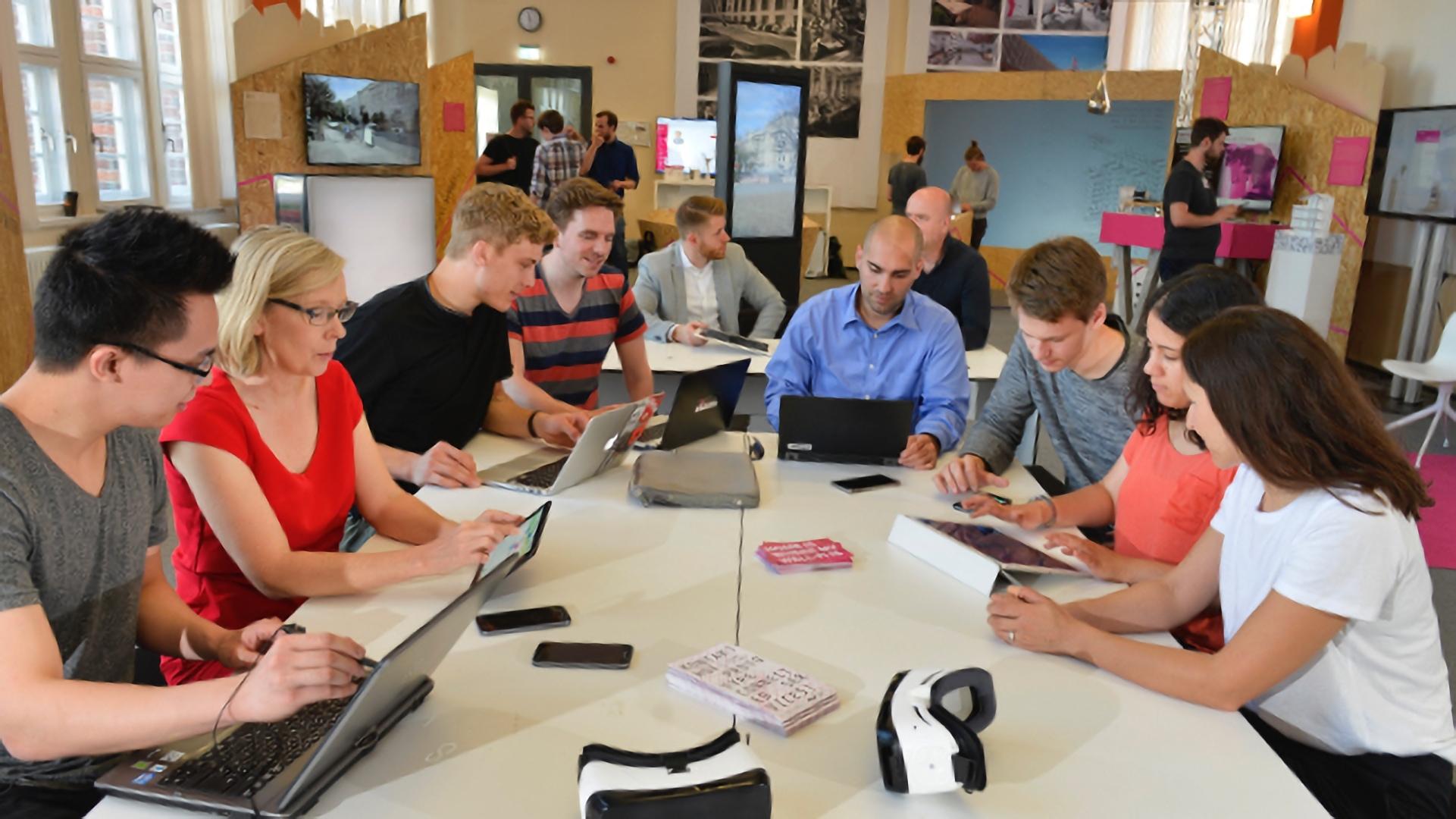 Teilnehmende eines Workshops sitzen mit Laptops gemeinsam am Tisch.
