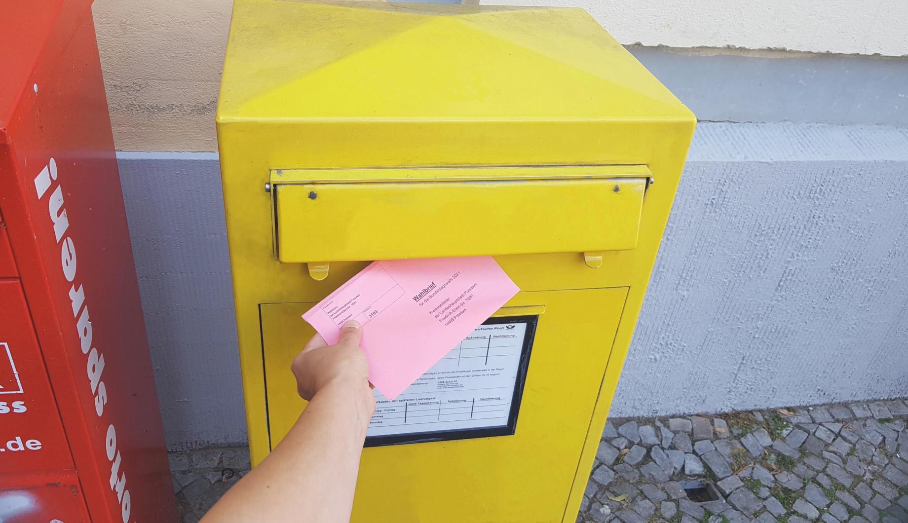 Rosa Wahlbrief wird in die Öffnung eines gelben Briefkastens geschoben