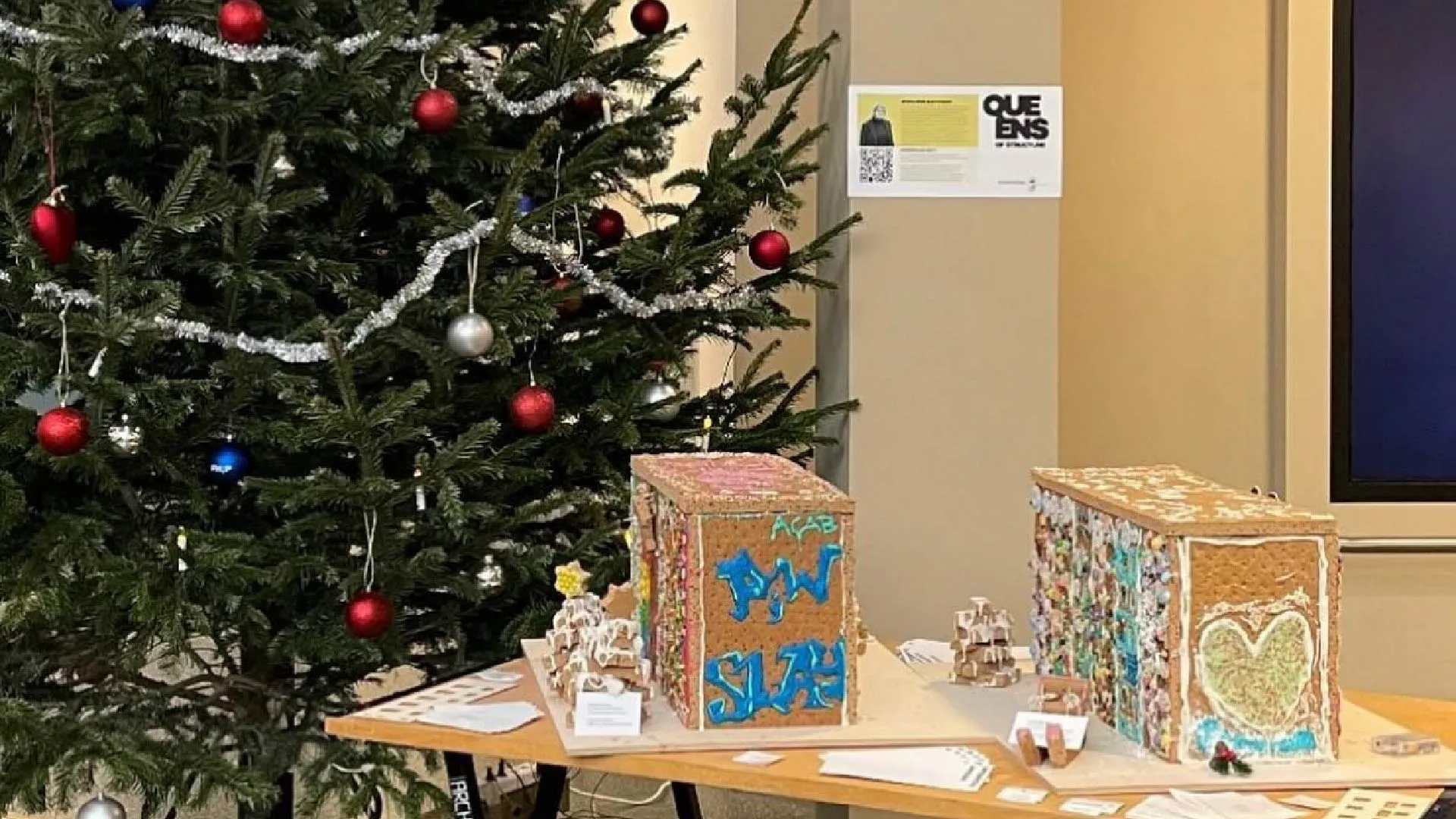 Zwei Lebkuchen-Häuser werden auf einem Tisch präsentiert, daneben ein Weihnachtsbaum