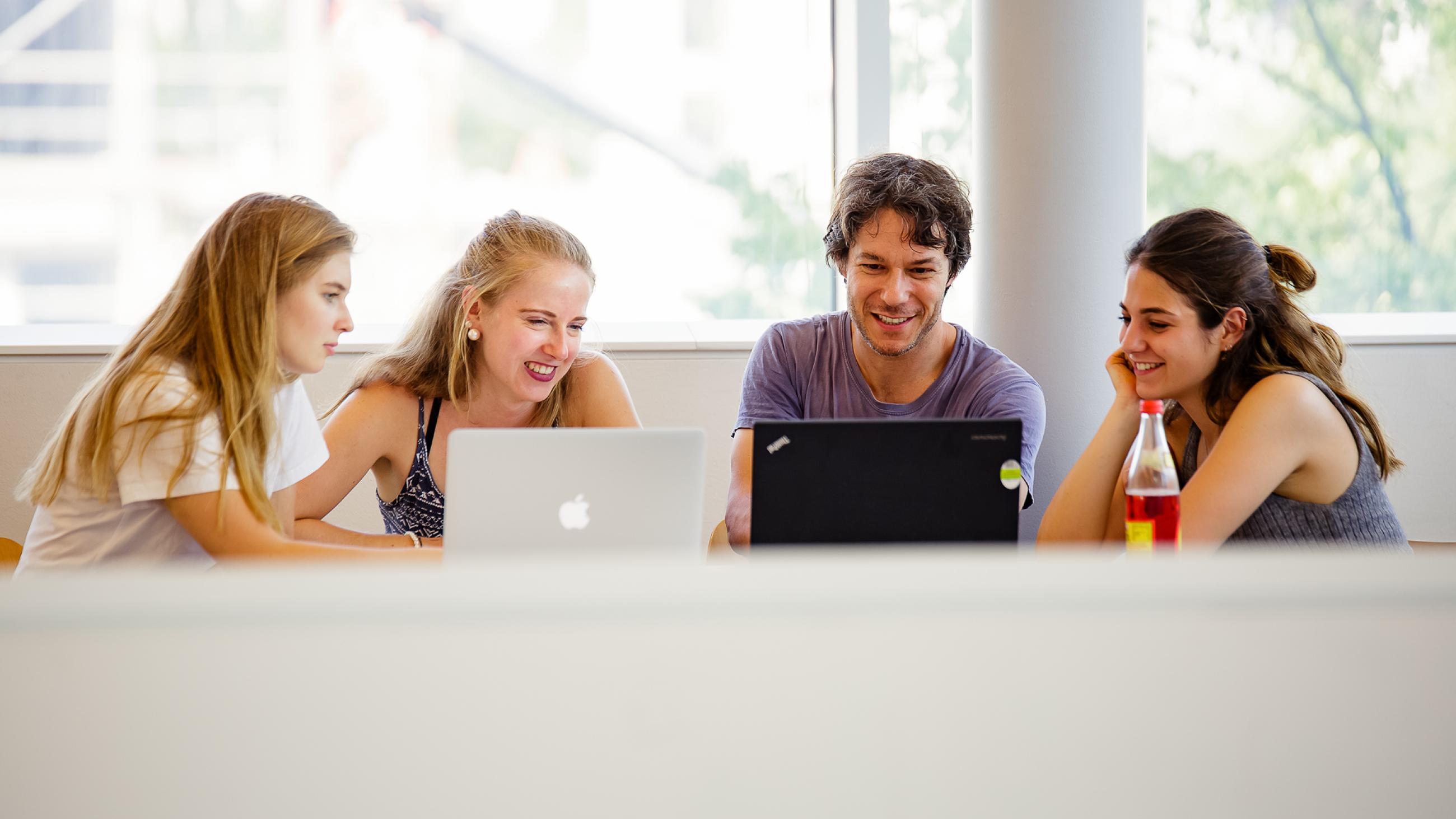Studierende sitzen vor einem Laptop und arbeiten zusammen