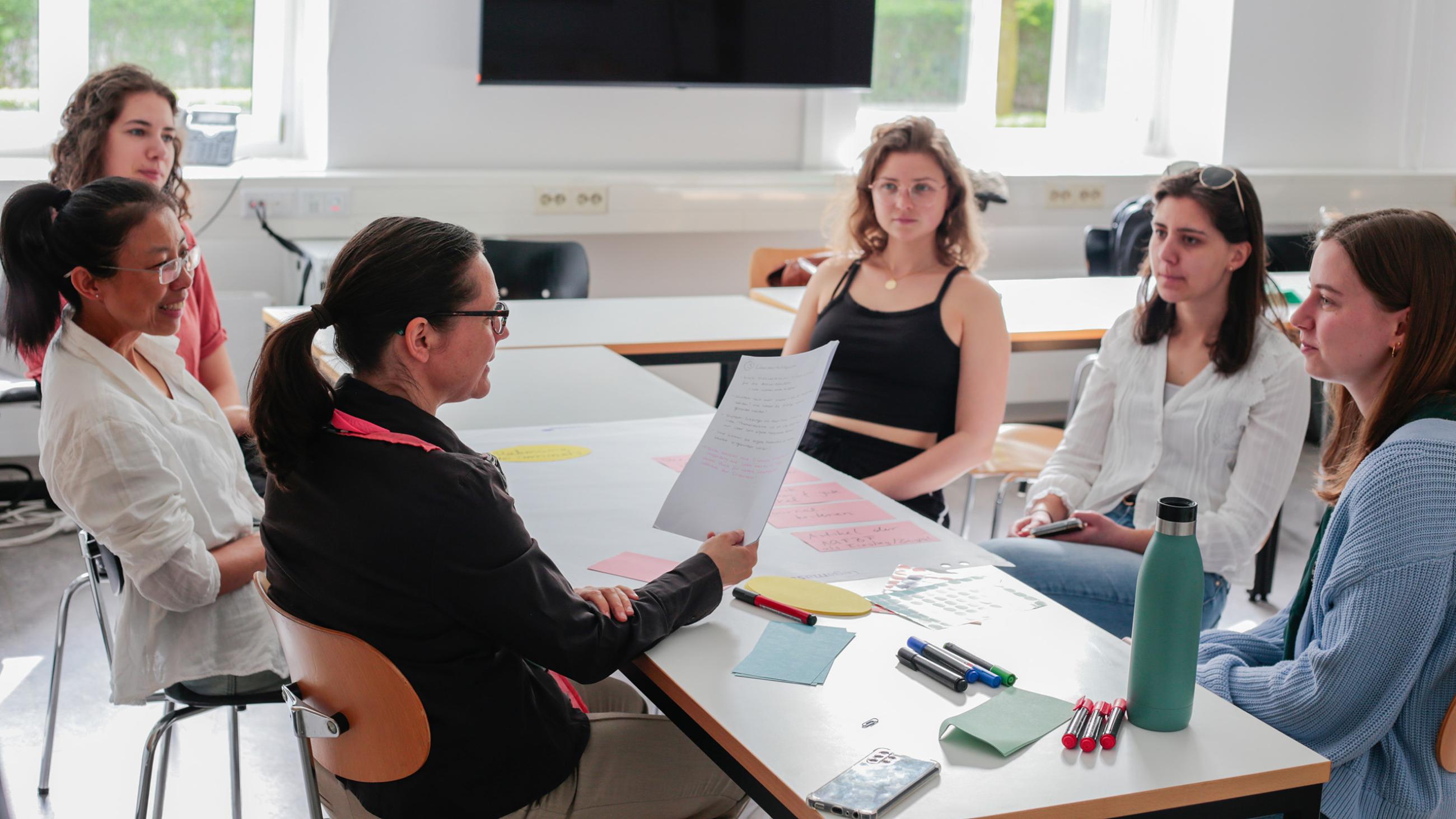 Fünf Studierende sitzen während eines Seminars mit Dokumenten an einem Tisch