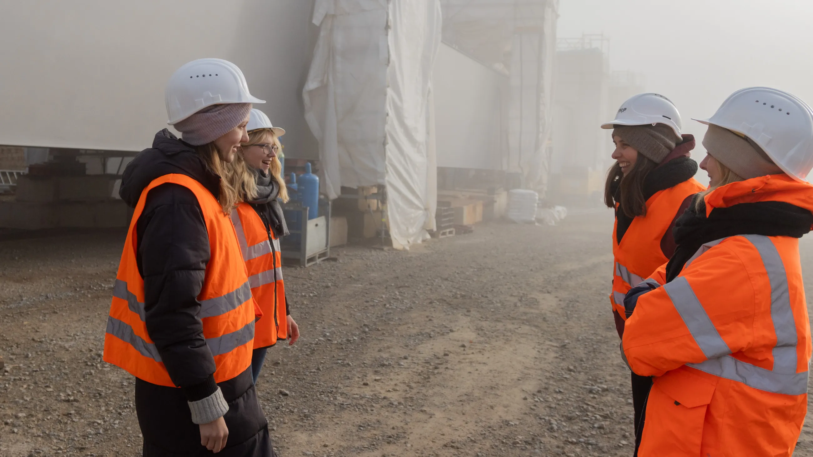 Vier Studierende stehen gut gelaunt mit Bauhelmen und Warnwesten auf einer Baustelle