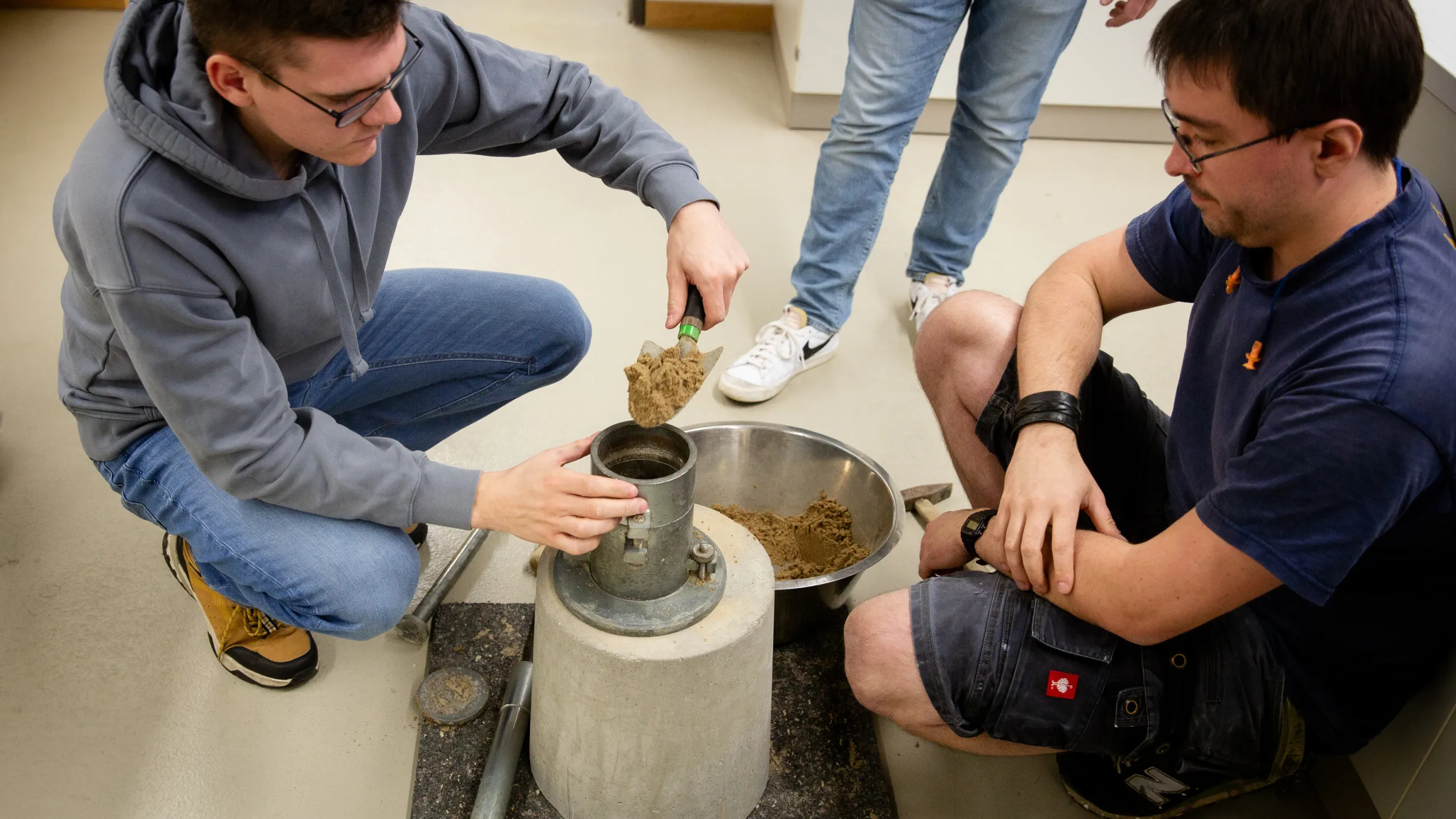 Studierende füllen einen Baustoff in einen Metallbehälter