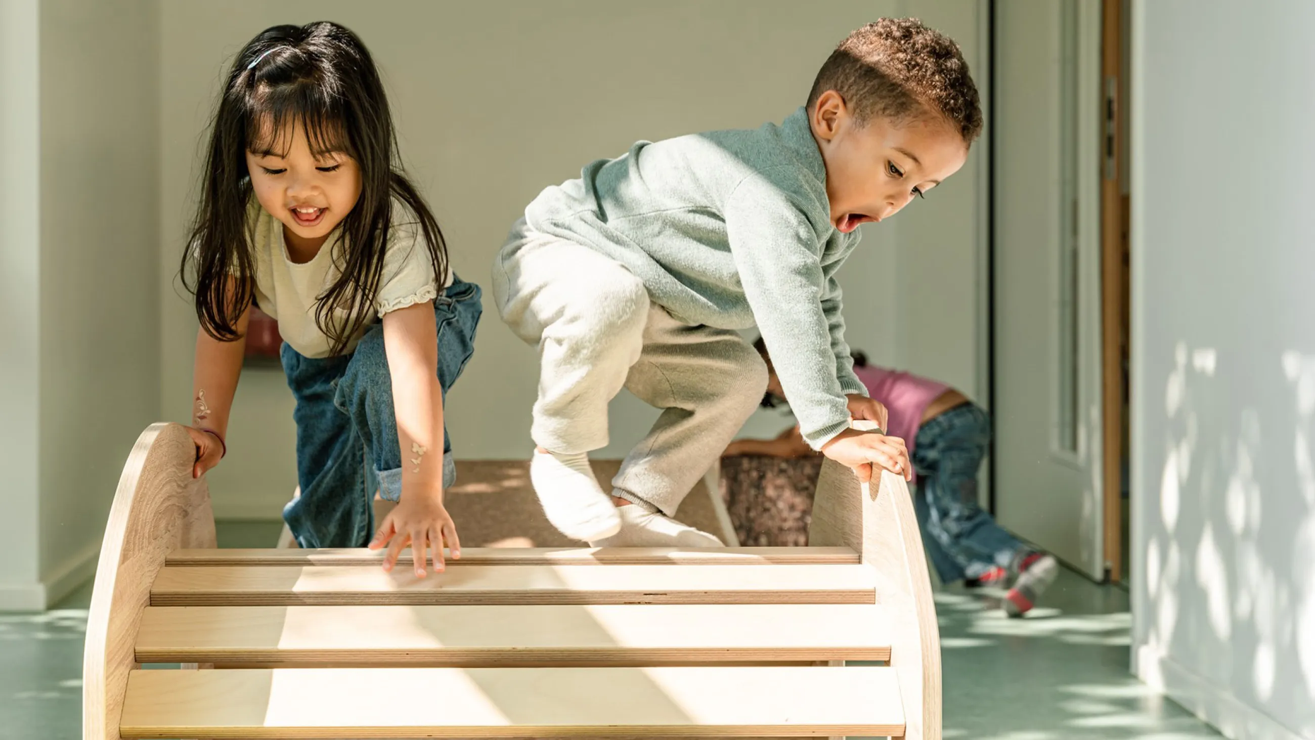 Zwei Kinder klettern auf einem Holzspielgerät in einem hellen Raum