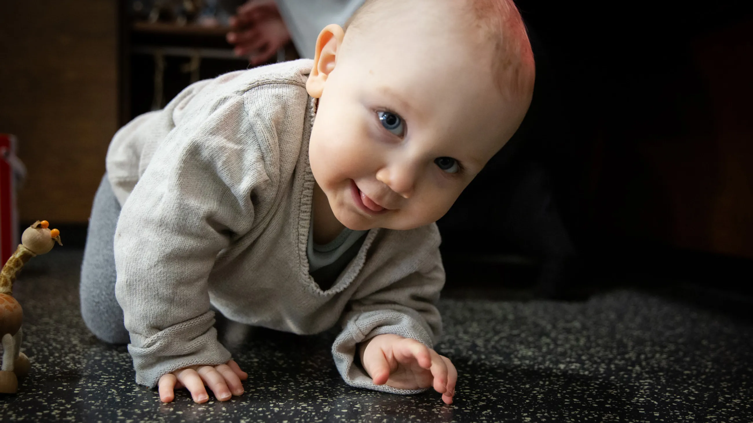 Kleinkind krabbelt auf einem dunklen, strukturierten Boden in einer Spielecke mit einem kleinen Spielzeugtier in der Nähe.