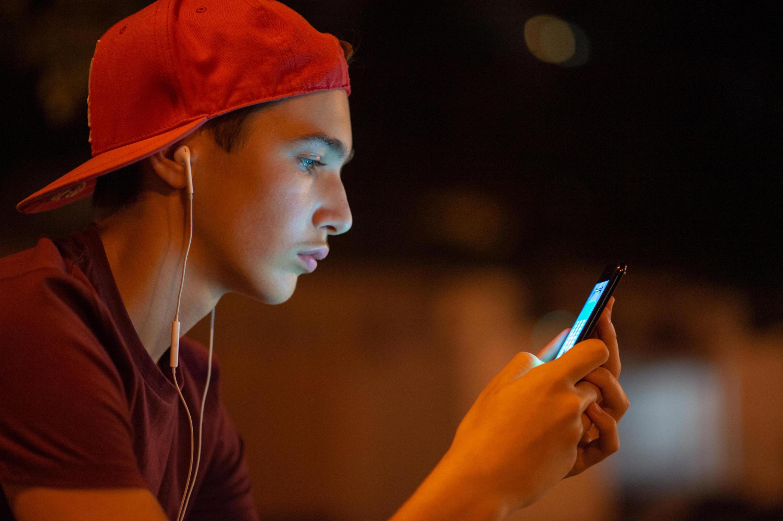 Junger Mann mit roter Basecap schaut auf sein Smartphone.