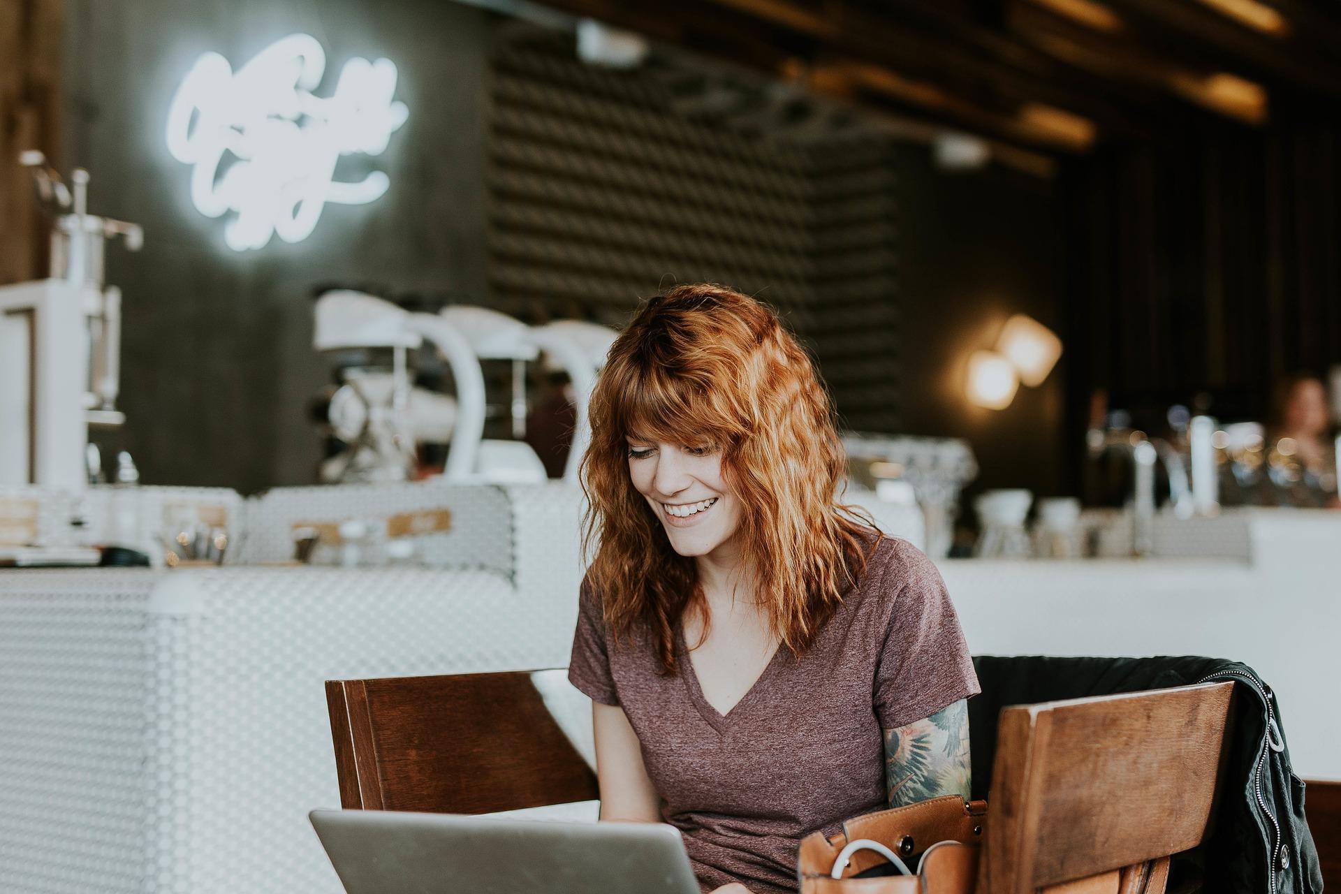 Frau sitzt lächelnd am Laptop im Café 