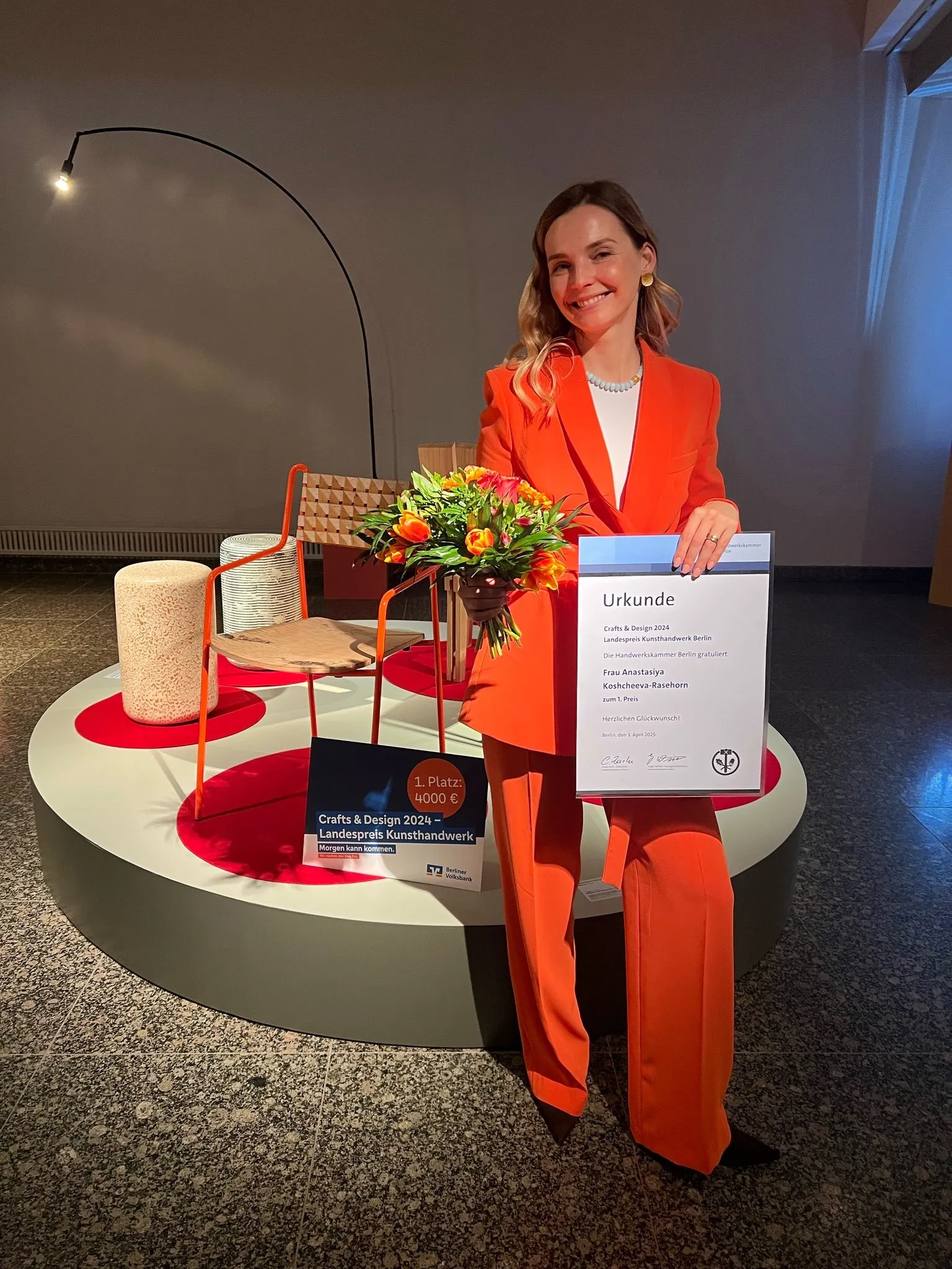 Frontalbild der Designpreis-Gewinnerin in rotem Anzug vor ihrem prämierten Stuhl