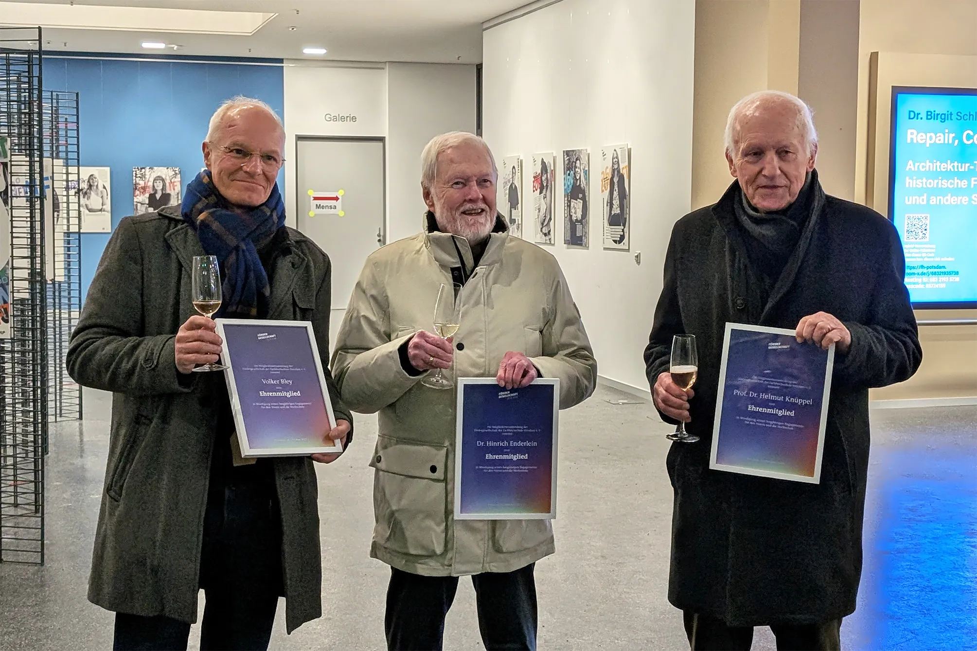 Drei Personen stehen nebeneinander und halten jeweils eine eingerahmte Urkunde in der Hand.