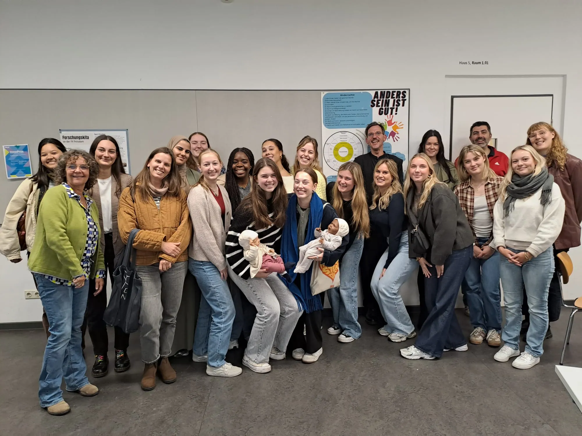 Gruppe von Studierenden in einem Raum, einige halten Puppen, im Hintergrund Plakate an der Wand.