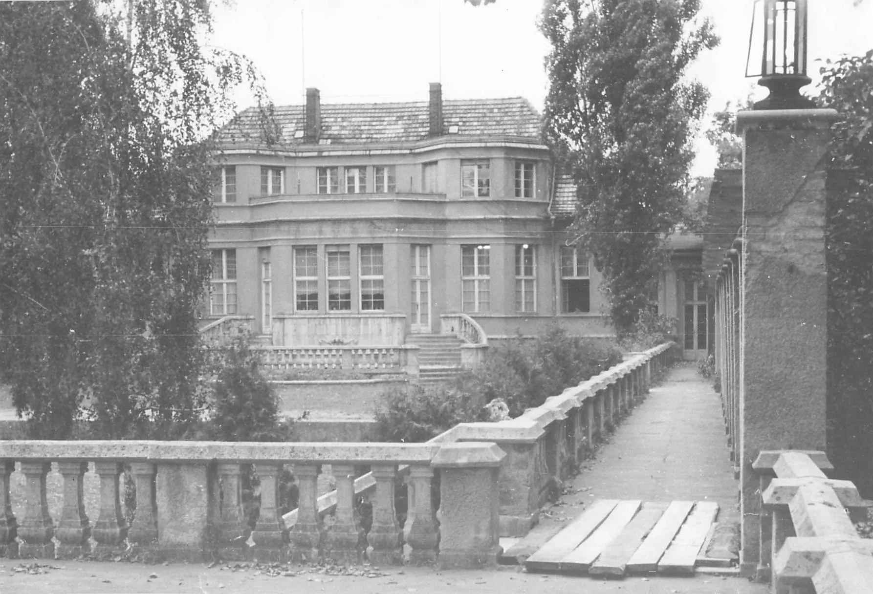 Blick auf die historische Villa Adlon mit Balustrade und Weg im Vordergrund umgeben von Bäumen