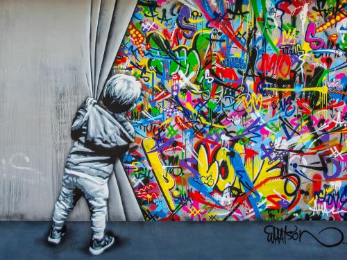 Bild eines Kindes, das einen grauen Vorhang aus Beton mit bunten Graffitis dahinter zur Seite zieht