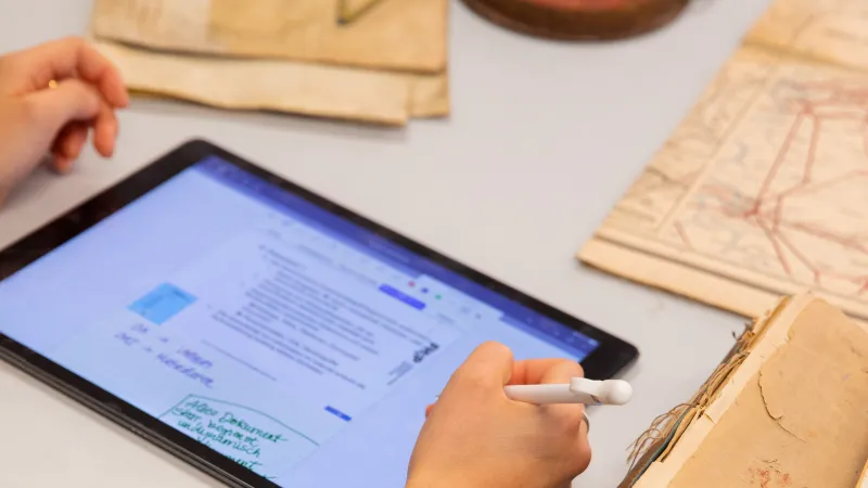 Eine Studentin macht sich Notizen auf einem Tablet neben historischen Dokumenten