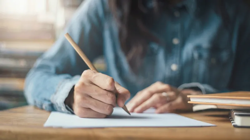 Eine Person schreibt mit Bleistift auf ein Blatt Papier